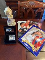 Wide shot showing all items on wooden table including figurine, royal magazines, and jewelry box with clock.