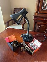 Photo of the entire set showing black gooseneck task lamp, hole punch, magnifying glass, stamp dispenser, and health balls laid out on wooden table.