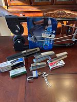 Overview of luggage cart, staplers with staples, master lock with key, and 3-hole punch on a wooden table.