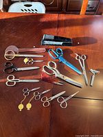 Lot of various scissors along with a black stapler and metal safety razor on a wooden table.