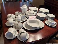 Overview of full set on dining table with stacks of plates, cups, carafe, sugar bowl, creamer, gravy boat and platters.