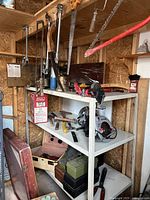 Shelf unit with various hand saws, clamps, hammer, mallet, Delta circular saw, wrenches, and several tool boxes beneath and on shelves in a workshop setting.