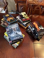 Three stacks of VHS tapes on a wooden table including titles like Century of Warfare and UFOs Are Real showing cover art and condition.
