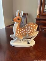 Front-side view of the glossy vintage Lomonosov porcelain deer figurine with spotted brown and white coloring on a wooden surface.