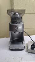 Front view of Breville BCG400 burr coffee grinder, showing silver body, bean hopper, adjustment dial, and collection area.