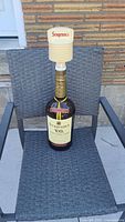 Full view of the large Seagram's V.O. whisky bottle with attached cream-colored plastic dispenser, placed on outdoor chair.