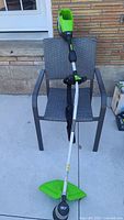 Full view of the Greenworks Pro 80V cordless string trimmer leaning on a chair showing the full shaft, handle, and cutting head with guard.