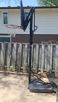 Full view of Lifetime portable basketball hoop on a driveway with wooden fence and house in background.