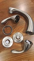 Price Pfister Roman tub faucet trim kit components including faucet spout, handles, and escutcheons shown disassembled on a wooden table surface.