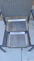 Two stainless steel BBQ grill baskets placed on a chair, showing perforated metal surfaces and metal handles.