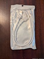 Three new Apple iPhone charging cables in white sealed plastic packaging shown spread out on a wooden surface