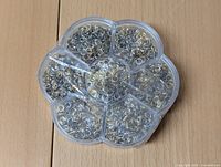 Top-down view of a round clear plastic container with seven compartments containing silver-tone metal crafting rings.