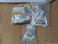 Photo showing gold-tone metal jump rings, small components, and chains packed in resealable plastic bags on a wooden surface.