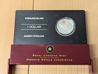Close-up of the sterling silver 1 dollar coin in black holder with the Royal Canadian Mint burgundy case partly visible.
