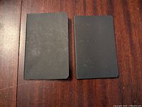 Front view of two small black Moleskine notebooks side by side on wooden surface.