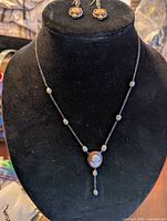 Full view of silver cameo necklace on black display bust with matching earrings displayed above.