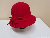 Front side view of the red wool cloche hat showing its rounded crown, short brim, and side flower decoration with tassel.
