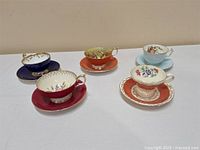 Five vintage Ansley teacups on matching saucers with various floral patterns and gold-trimmed rims and handles.