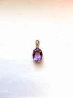 Top front view of 14K gold pendant showing large oval amethyst and small round diamond above, set in gold with hinged bale.