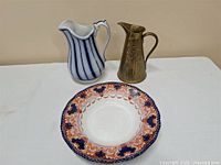 Photo showing all three items: a patterned Royal Doulton plate, ceramic striped jug, and brass jug.