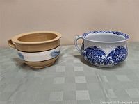 Two antique chamber pots side by side on a table, showing size and decoration.