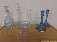 Five antique glass decanters and two blue glass candle holders arranged on a wooden surface.