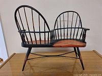 Front angled view of the wooden antique double seat doll's chair showing black frame and natural wood tones on seats.