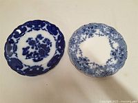 Both flow blue plates laid flat showing different blue patterns and scalloped edges