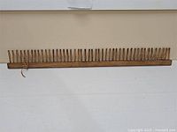 Full length view of the antique wooden heddle with multiple pegs for loom threading.