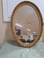 Oval mirror with ornate gold frame showing room reflection and some hazing on glass.