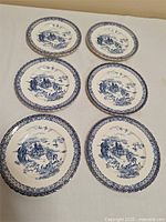 Six antique plates with blue pagoda pattern arranged on cream background