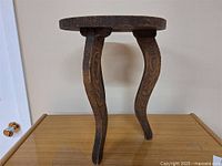 Side view of small wooden occasional table with three curved legs and dark aged finish.