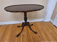 Full view of dark wood antique flip top table with scalloped edges and central pedestal base with tripod legs ending in claw feet.