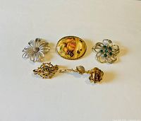 Five pieces of vintage costume jewelry including four brooches and one scarf clip arranged on white background.