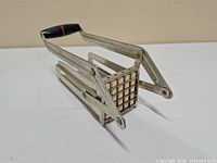 Metal German potato cutter angled view showing grid blade and handle.