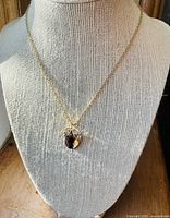 Gold tone necklace displayed on a beige fabric bust showing apple-shaped pendant with amber and clear rhinestones.