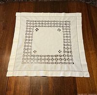 Full view of the square card table topper laid flat on a wooden surface, showing the overall design and cutwork border.