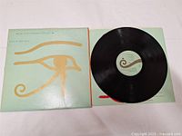 LP record partially out of green album cover displaying gold eye symbol and text. Record label visible with text and swirl logo.