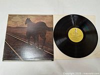 Photo of the LP vinyl record partially out of the album cover showing the black vinyl and yellow label.