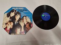 Octagonal album cover featuring the Rolling Stones band members and vinyl record with a blue label and green sticker.