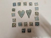 Overview of 22 handmade mosaic tiles arranged in a circle on a white background, featuring square and heart-shaped tiles with heart patterns.