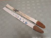 Photo of two guitar straps laid flat on a table to show full length and design. One has blue birds on white; the other a beige floral pattern on white.