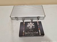 Closed silver aluminum poker chip case and boxed World Series of Poker wireless plug & play TV game on a flat surface.
