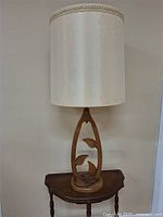 Full view of the retro wooden table lamp on a small wooden table against a white wall.