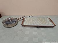 Salton electric hot tray and stainless steel egg poacher shown on a table with grey tablecloth.