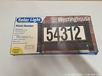 Box showing Westinghouse brand and product image of black plastic framed house number light with numbers 54312 displayed.