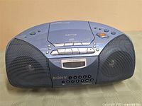 Front view of Sony boombox showing speakers, cassette controls, digital display and CD lid with MP3 label