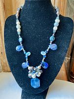 Full view of the vintage artisan necklace displayed on a black mannequin featuring blue facetted crystals, a cluster of freshwater pearls and polished stones, and a prominent sodalite pendant.