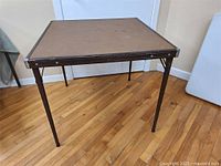 Full top and side view of the vintage folding card table showing brown top and metal legs.