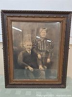 Full view of the framed vintage photo showing an elderly man seated and woman standing beside him.